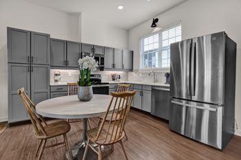 A modern kitchen with a large stainless steel refrigerator and wooden chairs around a round table.